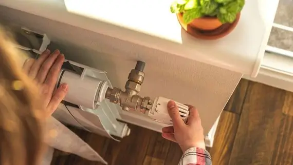 Frau dreht an Regler von Heizung | AL Oiltrans